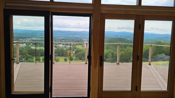 Una habitación con un gran ventanal corredero que da a un balcón con terraza de madera y vistas panorámicas del campo.