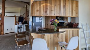 Una cocina compacta con muebles de madera, una isla central con taburetes de bar, un microondas y un refrigerador.