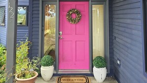 Una casa con una puerta de color rosa intenso, un balcón con barandilla y dos macetas a cada lado de la puerta.