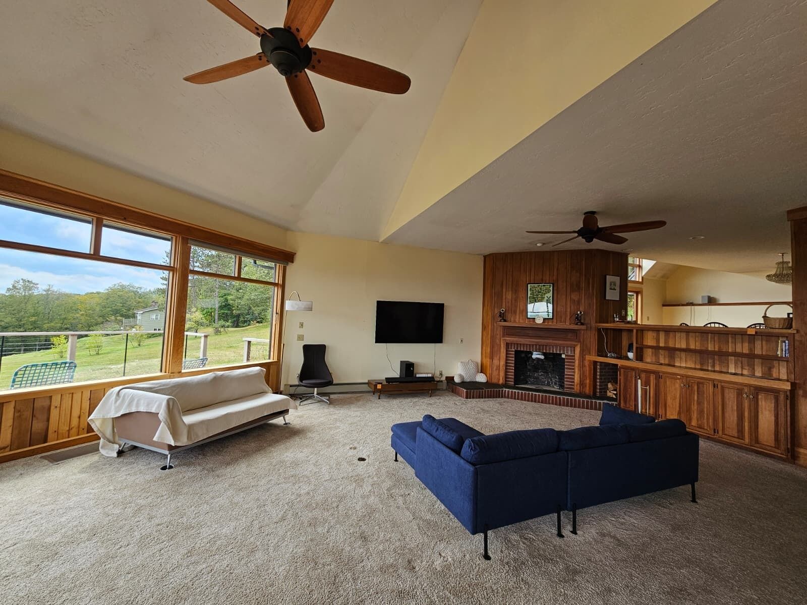 A spacious living room with a large window, a fireplace, a television, and a ceiling fan.