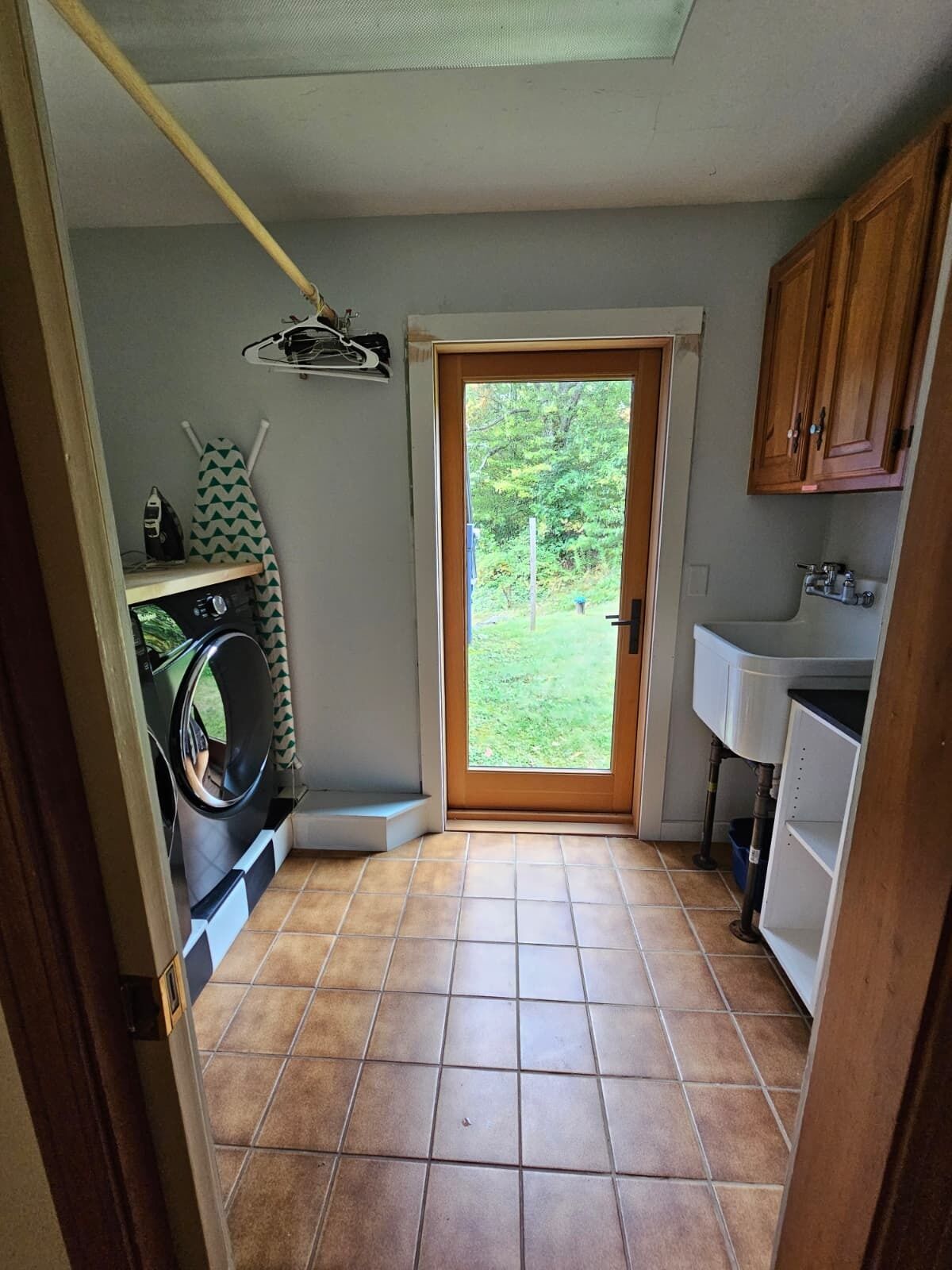 A laundry room with a washing machine, ironing board, and a sink.