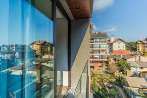 A modern building with large glass windows, a balcony, and a view of surrounding residential buildings.