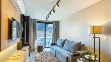 A modern living room with a sofa, a flat-screen TV, a coffee table, and a lamp.
