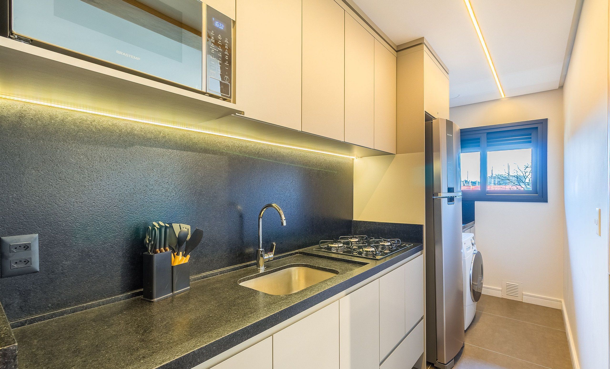 Une cuisine moderne dotée d’un four à micro-ondes encastré, d’appareils électroménagers en acier inoxydable et d’une fenêtre offrant une vue sur la ville.