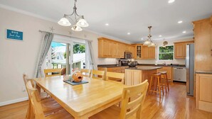 Een keuken met houten kastjes, een eettafel met stoelen en een kroonluchter.