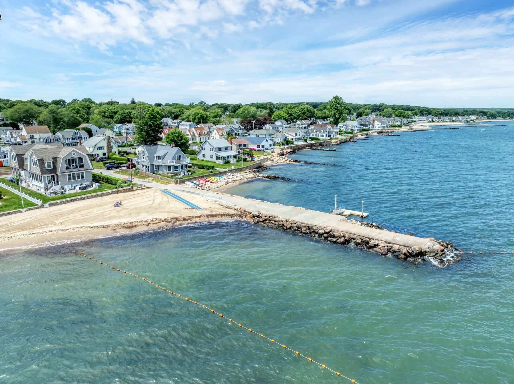 A coastal residential area with houses, a sandy beach, and a pier extending into the water.