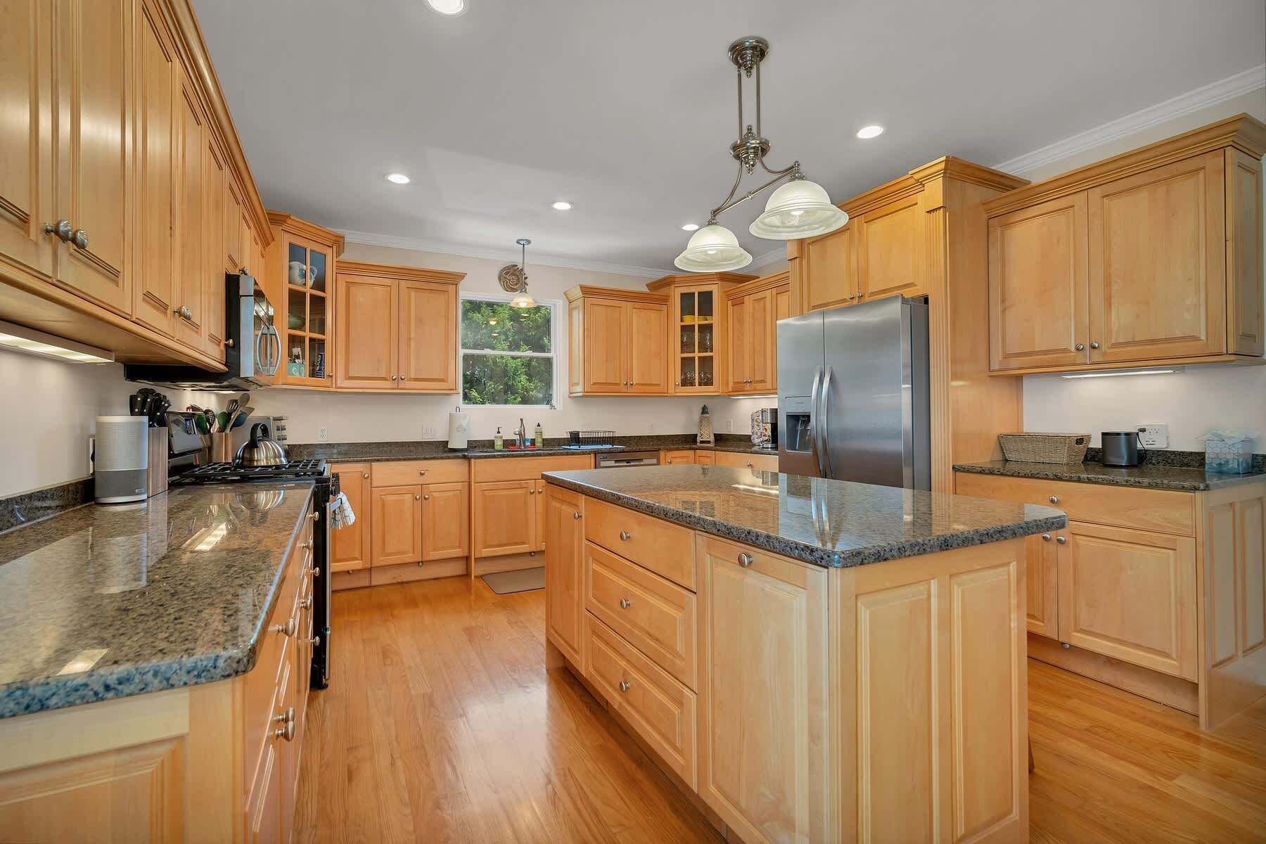 A kitchen with wooden cabinets, granite countertops, stainless steel appliances, and pendant lighting.