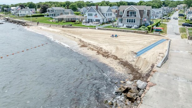 Een woongebied aan de kust met huizen, een strand en een betonpad.