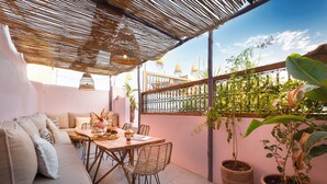 Eine gemütliche Terrasse mit einer Couch, einem Esstisch und Stühlen, umgeben von Blumentöpfen und einer Pergola.