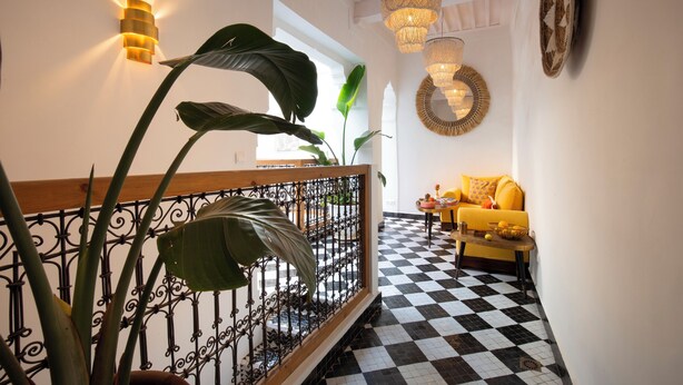 Eine Treppe mit schwarz-weiß kariertem Boden, einem gelben Sofa und einem Blumentopf.