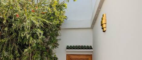 Een trap die leidt naar een kamer met een zwart-wit geruite vloer, een houten deur met ingewikkelde decoraties en een boom met groen blad.