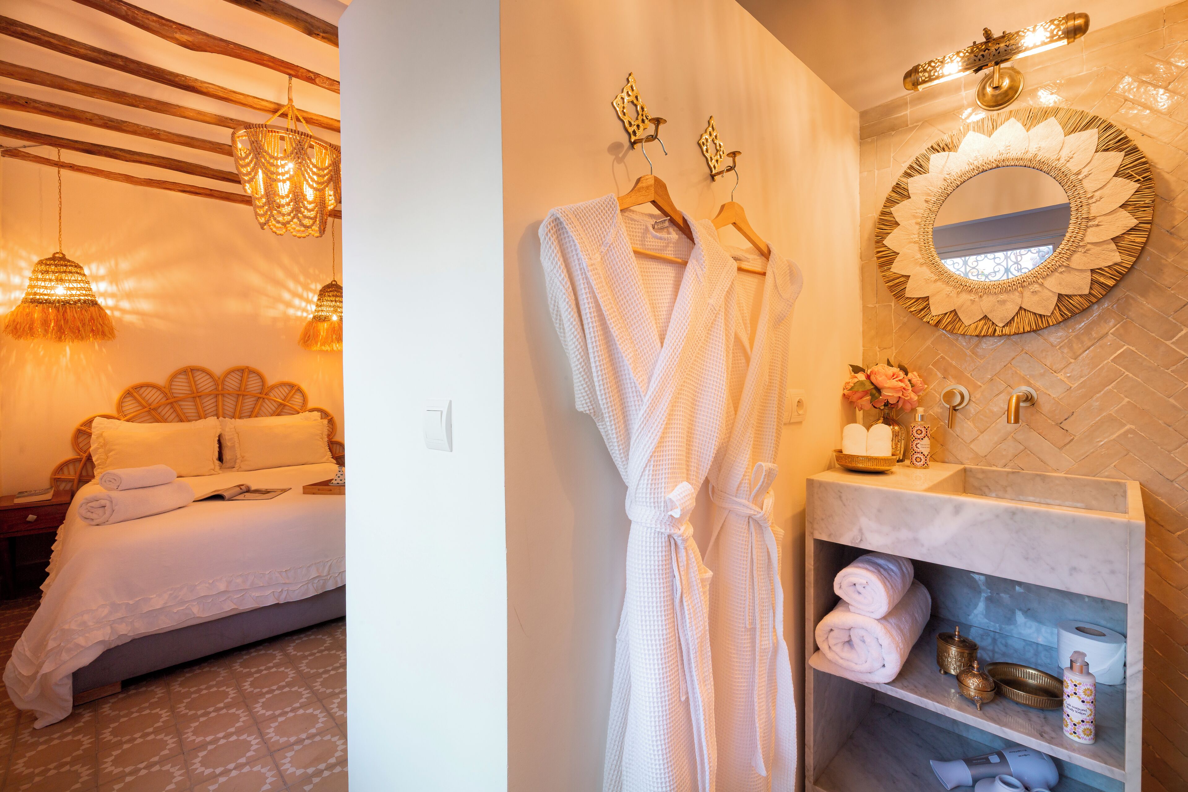 A hotel room with a bed, a robe hanging on a rack, a mirror, and a shelf with towels and toiletries.
