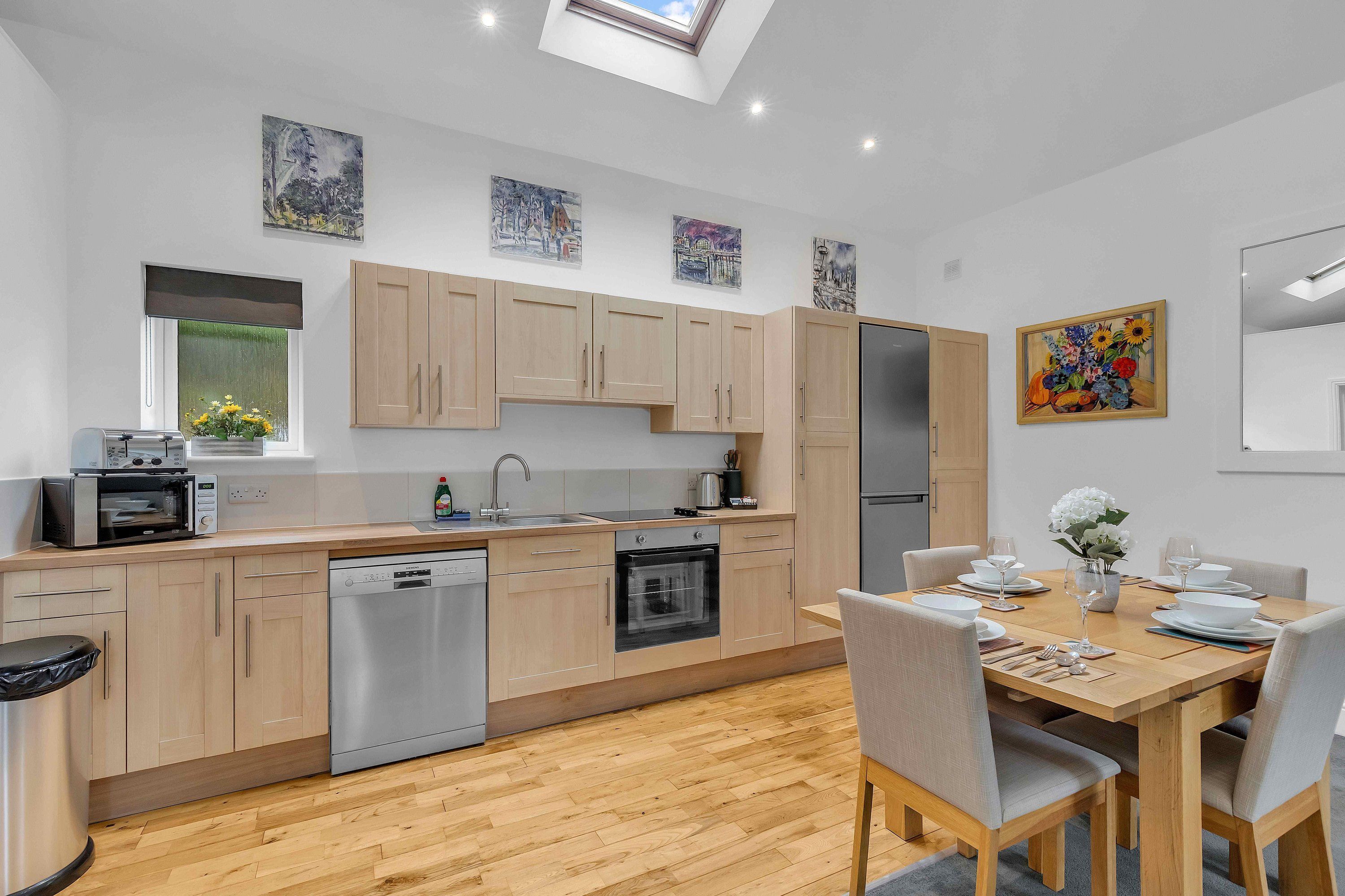 A modern kitchen with wooden cabinets, a dishwasher, and a dining area with a table set for four.
