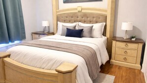 Ein ordentlich eingerichtetes Schlafzimmer mit einem großen Bett, zwei Nachttischen, einem Beistelltisch, einem Holzkopfende und einem Gemälde über dem Bett.