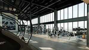A gym with various exercise equipment, large windows, and a high ceiling.