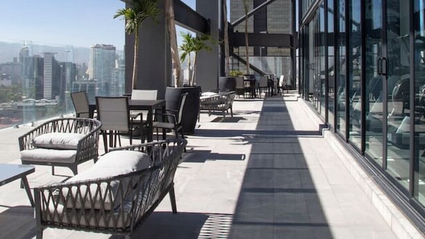 A rooftop terrace with outdoor seating, a view of the city skyline, and a tall building in the background.