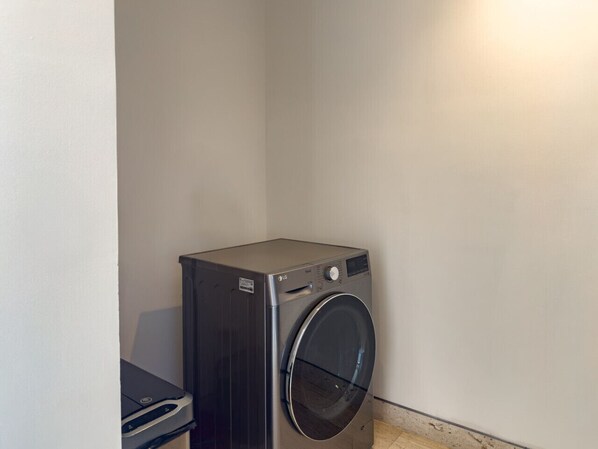 A compact, dark-colored washing machine in a corner of a room with plain walls.