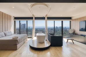 A modern living room with a large window, a round coffee table, a sofa, and a TV.