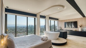 Une chambre moderne avec un grand lit, une baignoire sur pieds, une télévision et une vue sur la ville.