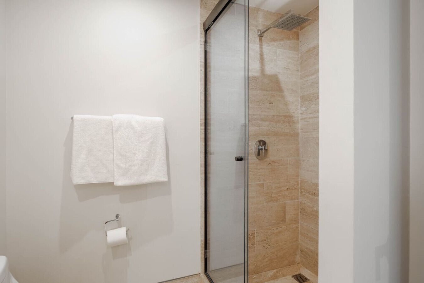 Ein modernes Badezimmer mit Duschkabine aus Glas und zwei weißen Handtüchern, die an der Wand hängen.
