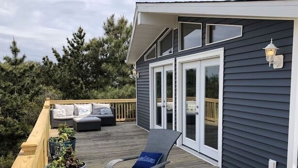 A deck with wicker furniture and potted plants, a sliding glass door, and a dark siding house.