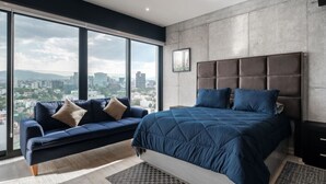 A modern bedroom with a large bed, a sofa, and a city view through large windows.