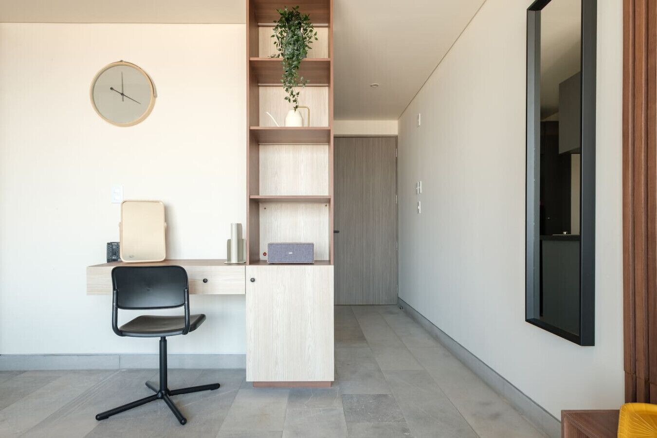 A modern office space with a desk, chair, laptop, bookshelf, and a clock on the wall.