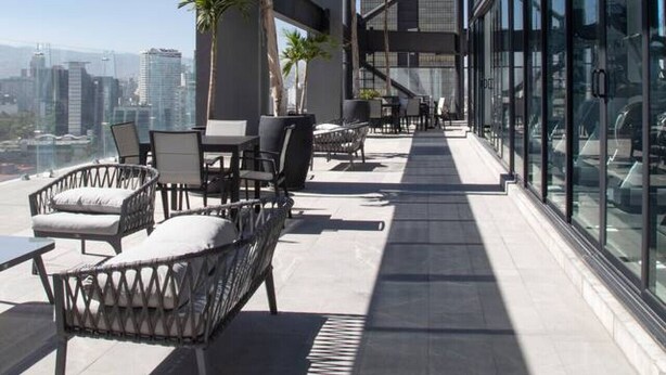Een terras op het dak met buitenmeubels en uitzicht over de stad.