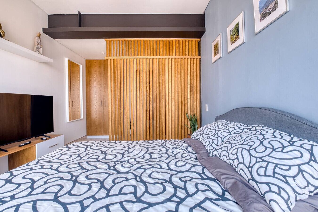 Une chambre moderne avec un grand lit, une télévision et un mur recouvert de lattes de bois.
