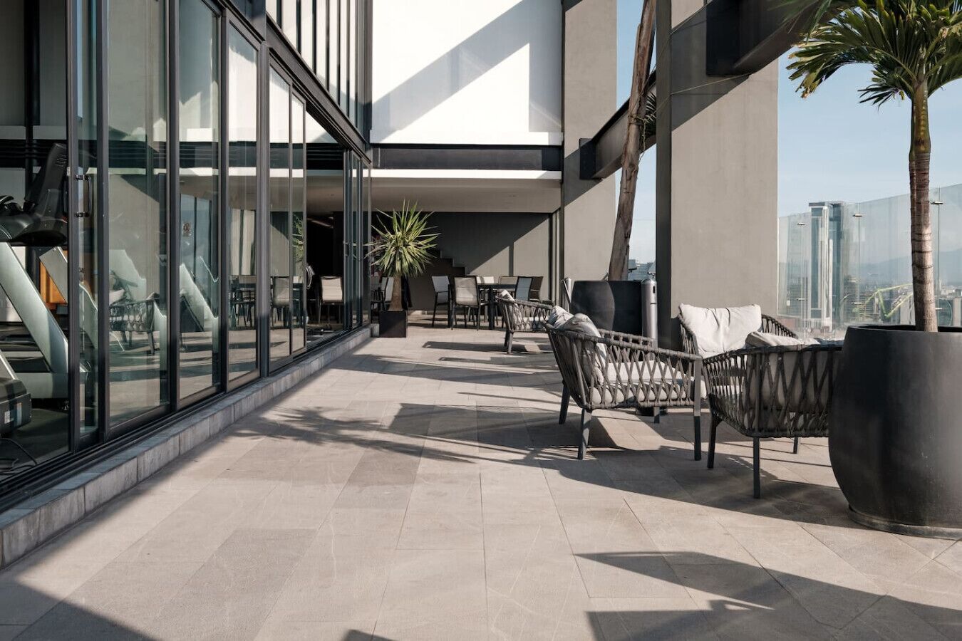 Un espace de détente extérieur moderne, doté de murs en verre, de sièges et d’une plante en pot.
