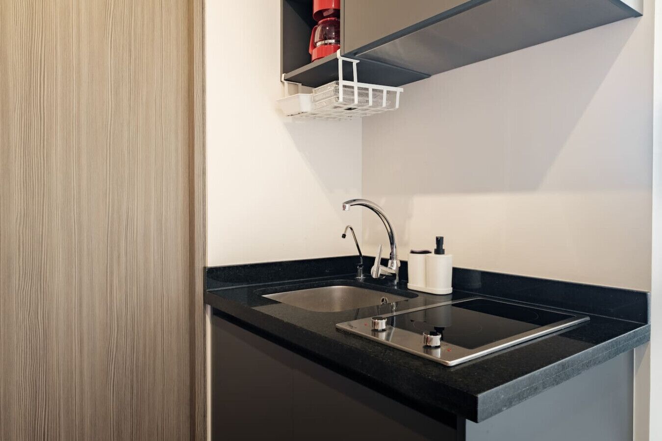 Une cuisine moderne avec un plan de travail noir, un évier en acier inoxydable et un appareil électroménager rouge fixé au mur.