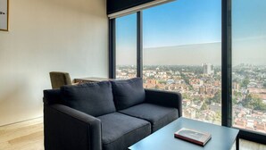 Una sala de estar moderna con un sofá negro, una mesita y un ventanal con vistas a la ciudad.