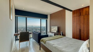 Una habitación de hotel moderna con una cama grande, un escritorio, una silla, un televisor y vistas de la ciudad.