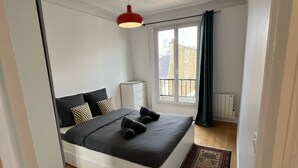 A modern bedroom with a bed, a red pendant light, a window with curtains, and a view of the outside.