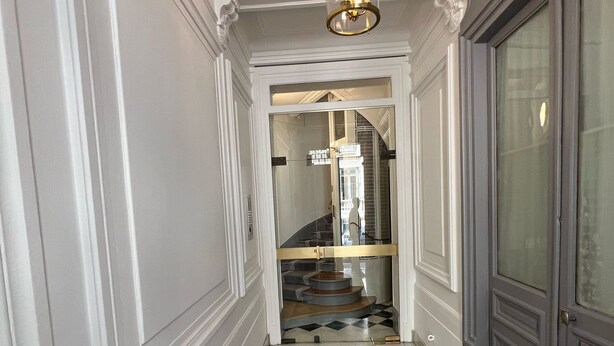 A hallway with a checkered floor, a brown rug, and a chandelier.