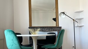 A modern dining area with a glass table, teal chairs, a large mirror, and a floor lamp.