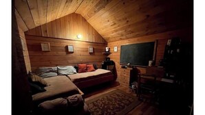 Una habitación de cabaña acogedora, con techo de madera, una cama, un escritorio y una silla.