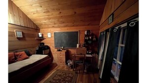 Acogedora habitación tipo cabaña con cama, escritorio, silla, una alfombra pequeña y ventana con cortinas.