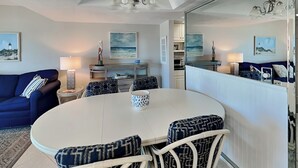 A dining area with a round table, four chairs, and a central coffee table. - Bent Palm 202 | Oceanfront Condo with Balcony Views, Pool + Beach Access (Ormond Beach)