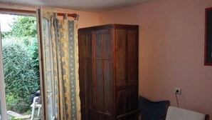 A room with a wooden table, a blue chair, a wardrobe, and a door leading to a garden. - No luxury accommodation For two people (Concarneau)