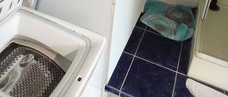 A laundry area with a washing machine, a drying rack, and a box of detergent on the counter.