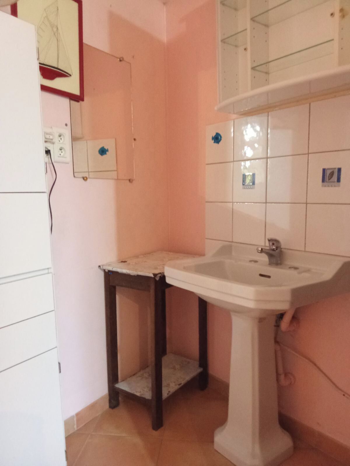 Un baño pequeño con un lavabo blanco, un espejo y una mesita.