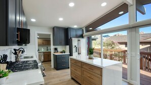 A modern kitchen with dark cabinets, a white countertop, and a large window overlooking a deck.