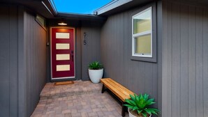 A house with a red door, a bench, and two potted plants.