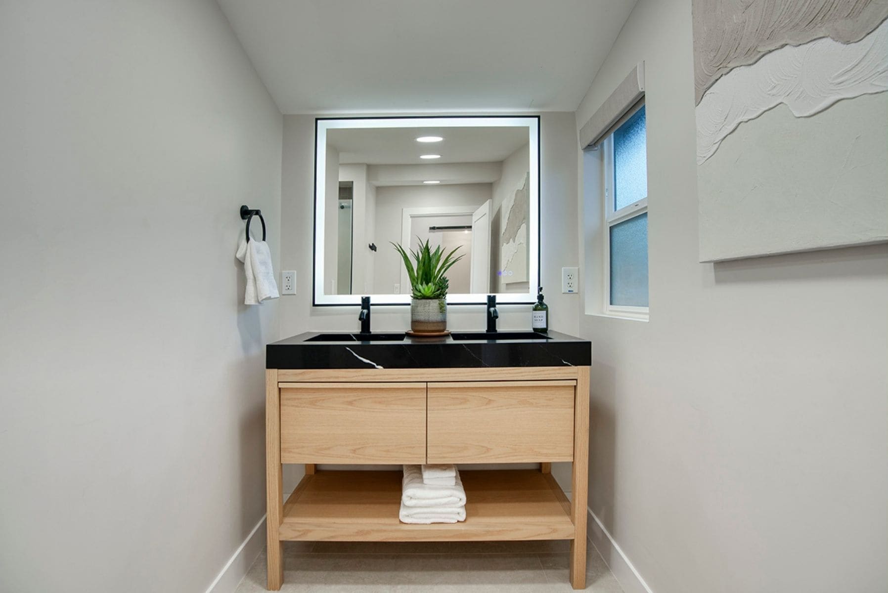 Une salle de bain moderne avec un plan de toilette noir, un meuble-lavabo en bois et un grand miroir.