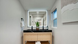 A modern bathroom with a black countertop, wooden vanity, and a large mirror.