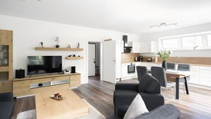 A modern living room with a flat-screen TV, a sofa, a coffee table, and a dining area with a table and chairs. - Apartment 1, ground floor, 85 sqm, 2 bedrooms, for up to 4 people (Potsdam)