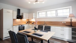 A modern kitchen with white cabinetry, a wooden countertop, a dining table with chairs, and a window with natural light. - Apartment 1, ground floor, 85 sqm, 2 bedrooms, for up to 4 people (Potsdam)