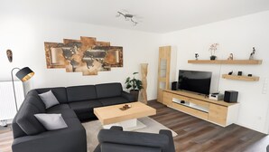 A modern living room with a sectional sofa, a coffee table, a TV, and wooden shelves. - Apartment 1, ground floor, 85 sqm, 2 bedrooms, for up to 4 people (Potsdam)