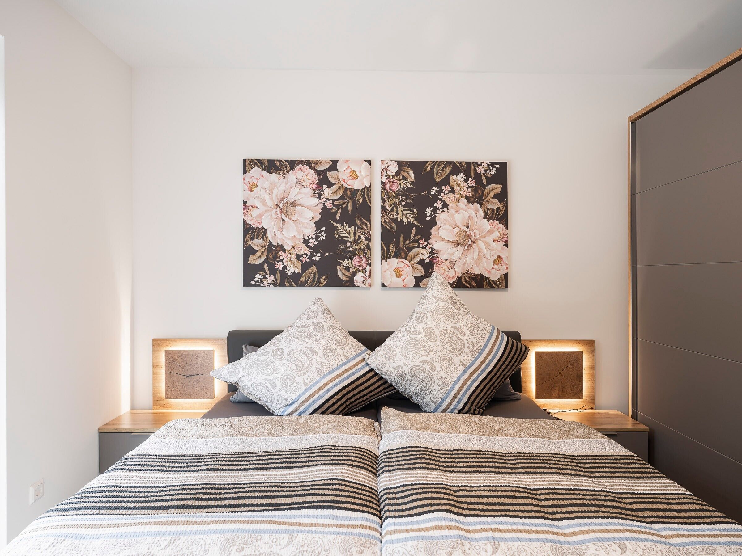 Een slaapkamer met een bed, twee nachtkastjes, een wandlamp en twee aan de muur hangende schilderijen.